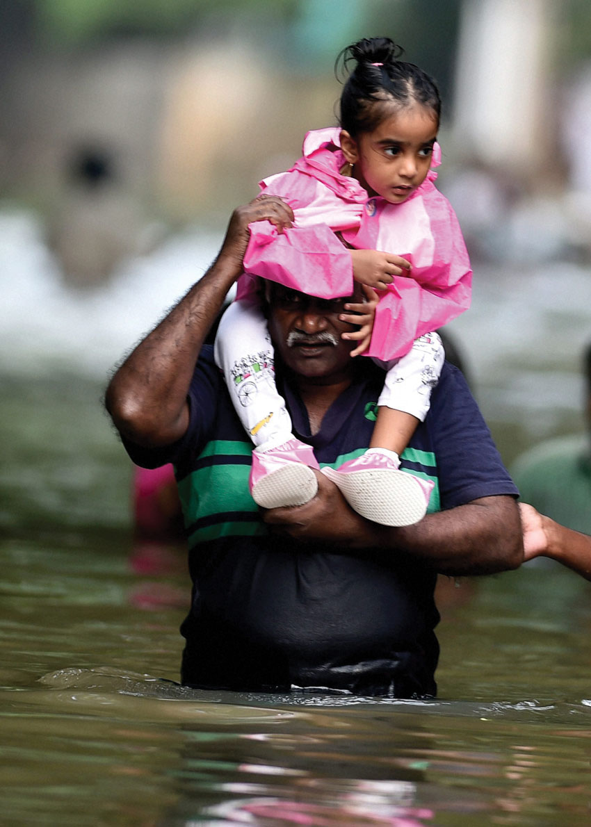 People carry children on their shoulders as they wade through flood waters in rain-hit Chennai, Dec. 3. (Press Trust of India)