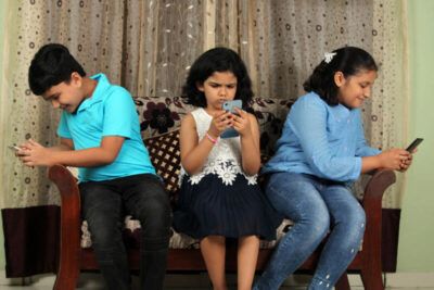Technology spoiling Indian childhood - kids are busy using smartphone while sitting on a couch, indoors.